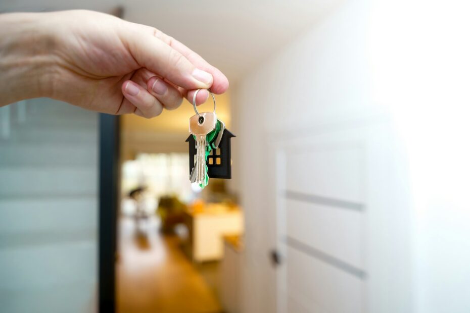 Hand holding house keys in front of a rental home entrance