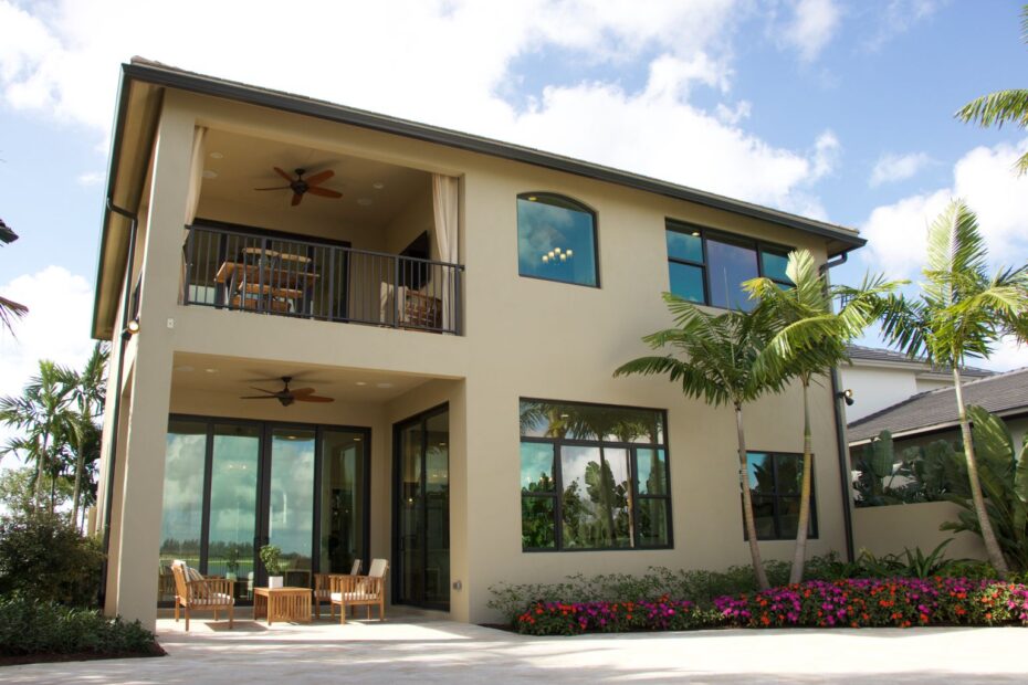 Two-story stucco home with balconies and palm trees under a blue sky