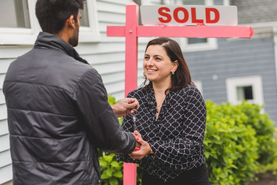 Real estate agent handing house keys to a client in front of a sold sign